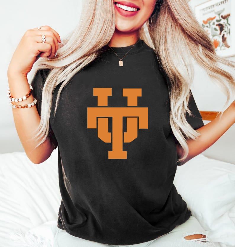 May include: Black t-shirt with a burnt orange graphic of the letters "TT" stacked on top of each other. The shirt is a crew neck style and appears to be made of a soft material. The graphic is centered on the front of the shirt.