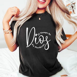May include: Black t-shirt with the words "Dios Es Perfecto" in white script. The shirt has a crew neck and short sleeves. The text translates to "God is perfect".