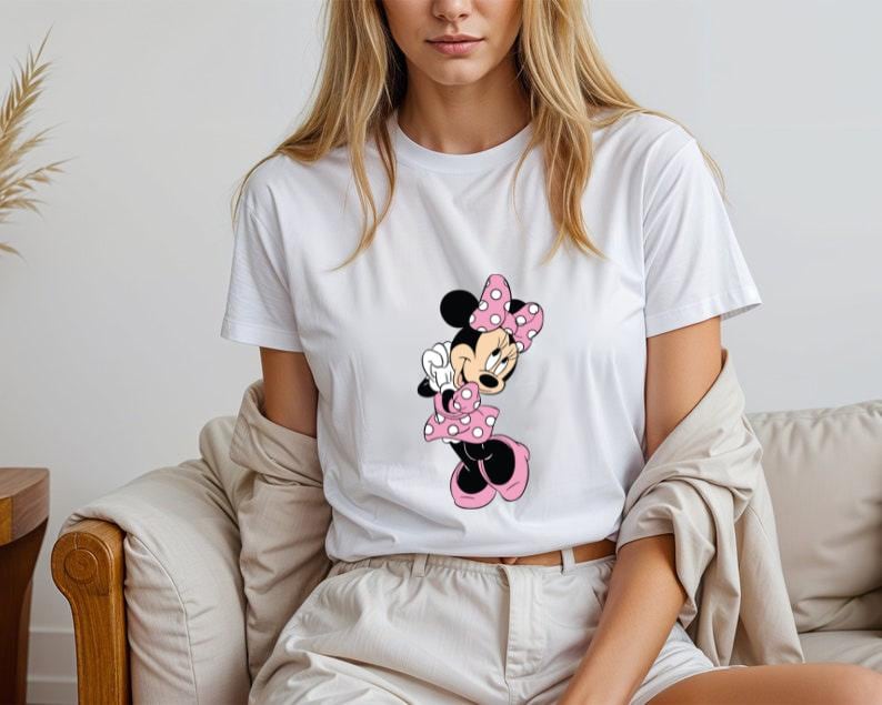 May include: White t-shirt with a pink and black Minnie Mouse graphic. Minnie Mouse is wearing a pink bow and a pink polka dot dress.
