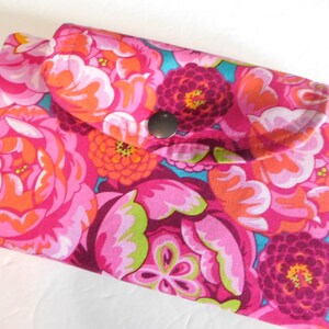 May include: A pink fabric wallet with a floral print and a silver button closure. The flowers are pink, orange, and purple.
