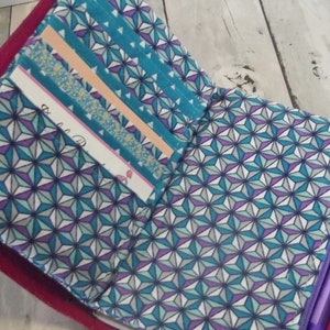 May include: A purple notebook with a zipper closure and a teal and purple geometric pattern. The notebook has several pockets on the inside for holding cards, notes, and other small items.