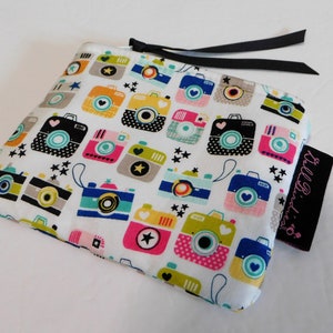 May include: A white zippered pouch with a repeating pattern of colorful cameras and black stars. The cameras are in various colors including pink, blue, yellow, and green. A black ribbon is attached to the zipper. A black tag with pink text is on the side.