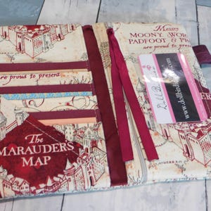 May include: Open, cream-colored fabric wallet featuring a map design with red accents. The wallet has multiple card slots and a burgundy ribbon closure. Text on the wallet includes "The Marauders Map" and "Messrs Moony, Wormtail, Padfoot & Prongs are proud to present."