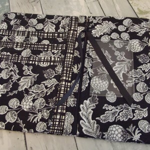 May include: Black and white fabric journal cover with a botanical pattern. The cover is open, revealing pockets and a clear window. A dark purple pen is secured on the right side. The fabric design features leaves, acorns, and other natural elements.