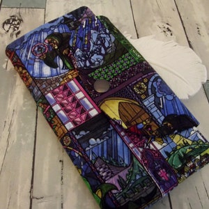 May include: A fabric wallet with a stained-glass window design. The wallet features a snap closure and a colorful pattern with figures, buildings, and a stormy sky in shades of blue, purple, and green.