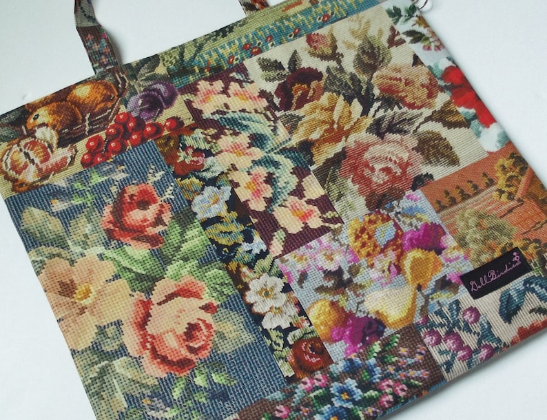 Pode incluir: Uma bolsa tote de patchwork com um design floral. A bolsa &eacute; feita de um tecido com textura tecida e apresenta uma variedade de cores, incluindo vermelho, verde, azul e amarelo. A bolsa tem uma &uacute;nica al&ccedil;a e uma pequena etiqueta que diz "Lille Prinzess".