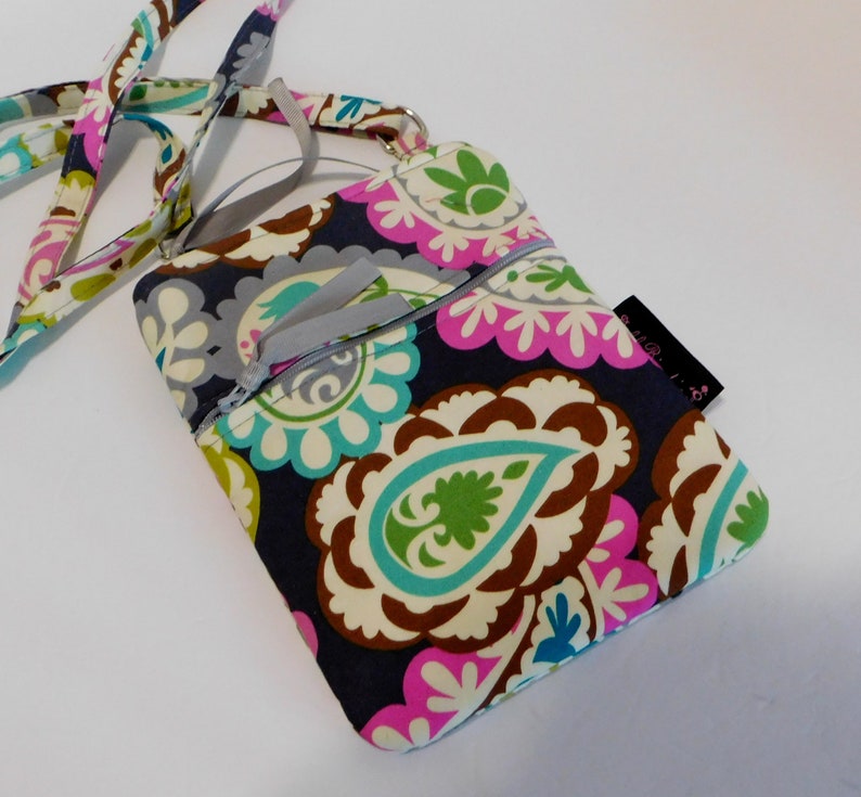 K&ouml;nnte beinhalten: Eine kleine Umh&auml;ngetasche mit Paisley-Muster, Rei&szlig;verschluss und langem verstellbarem Trageriemen. Die Tasche ist aus dunkelblauem Stoff mit verschiedenen Farben, darunter Pink, Gr&uuml;n und Braun.