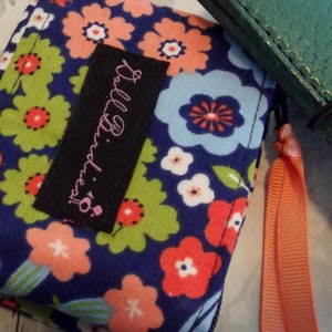 May include: A small blue fabric pouch with a floral print and a black label that says "Lilly Pulitzer". The pouch has a bright orange zipper pull.