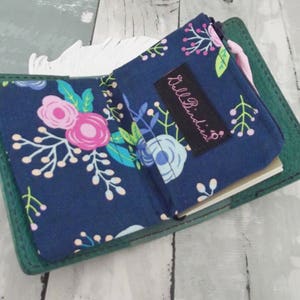 May include: A green leather notebook with a blue and floral fabric cover. The notebook has a zippered pocket on the front with a black label that says "Lili Birds".