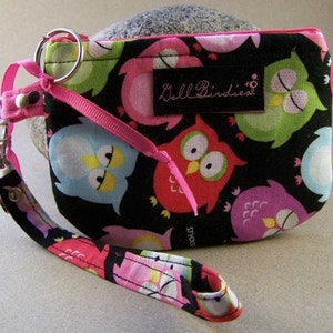 May include: A black zippered pouch with a pink strap and a silver key ring. The pouch is decorated with a colorful owl print and the text "Bella Birdles".