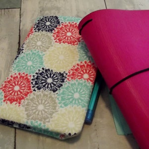 May include: A pink binder with a black elastic band and a floral patterned fabric cover. The binder is closed and has a blue pen sticking out of it.