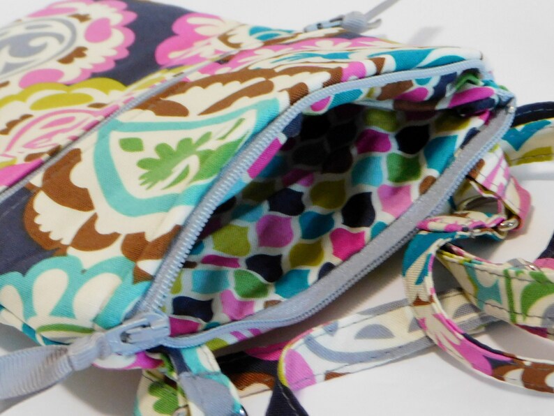 K&ouml;nnte beinhalten: Eine kleine, farbenfrohe Umh&auml;ngetasche mit Muster, Rei&szlig;verschluss und langem Trageriemen. Die Tasche ist aus Stoff und hat ein Paisley-Muster.