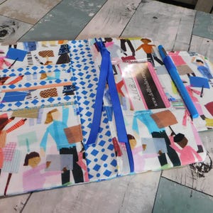 May include: A fabric organizer with a colorful print featuring figures and geometric patterns. The organizer has multiple pockets, a clear ID holder, and a blue pen. Blue ribbons are attached to the zipper.