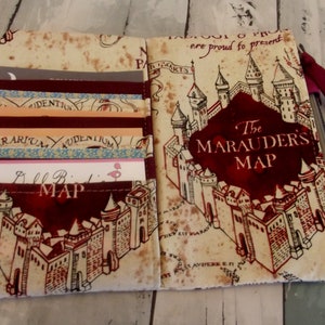 May include: A beige fabric wallet with a red and black print of the Marauder's Map from the Harry Potter series. The wallet has multiple card slots and a flap closure.