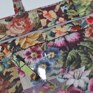 Pode incluir: Uma bolsa tote com padr&atilde;o floral, fecho de correr e uma janela de pl&aacute;stico transparente. A bolsa tem um puxador de z&iacute;per prateado com um chaveiro e uma al&ccedil;a verde e amarela.