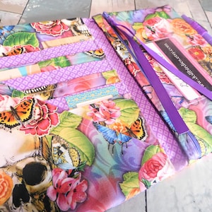 May include: Open floral print wallet with a skull, butterflies, and roses in shades of purple, pink, orange, and green. The wallet has multiple card slots and a pen holder. The text "www.dollholics.etsy.com" is visible.