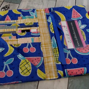 May include: A blue fabric wallet with a zipper closure and a variety of pockets. The wallet features a colorful fruit print with pineapples, bananas, watermelons, and cherries. The wallet has a blue ribbon and a clear plastic business card holder with the text "DollBirdies Etsy.com" and "www.dollbirdies.etsy.com".