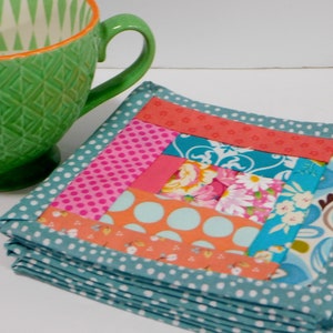 May include: A stack of colourful fabric coasters with a patchwork design. The coasters are made of various fabrics in shades of pink, orange, blue, and white. The coasters are edged with a teal fabric with white polka dots.