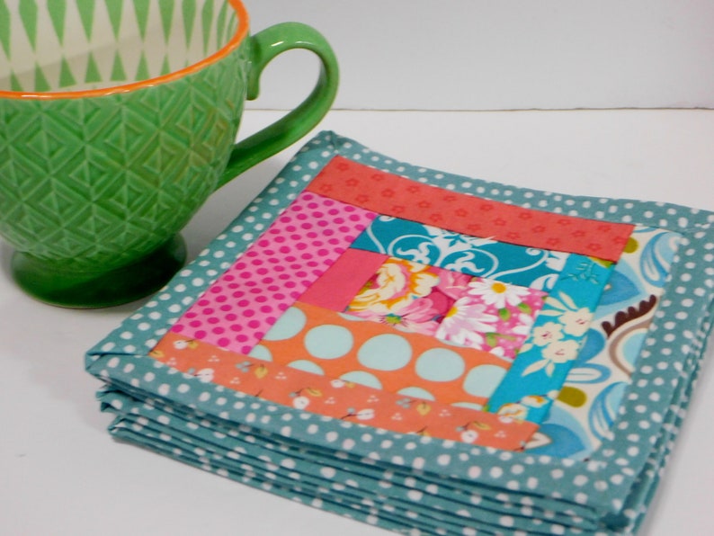 May include: A stack of colourful fabric coasters with a patchwork design. The coasters are made of various fabrics in shades of pink, orange, blue, and white. The coasters are edged with a teal fabric with white polka dots.