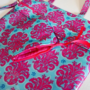 May include: A turquoise and pink tote bag with a damask pattern. The bag has a zippered pocket on the front and a top zipper closure.