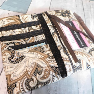 May include: Open, paisley-patterned wallet in shades of brown, black, and cream. The wallet features multiple card slots and a zippered compartment. A brown pen and a business card with the website "www.dollbirdies.com" are visible.