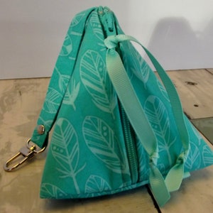 May include: A turquoise zippered pouch with a white feather pattern and a turquoise ribbon tie. The pouch has a gold metal key ring.