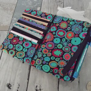 May include: A black fabric wallet with a colorful, abstract pattern of circles and swirls. The wallet has a zippered pocket on the side and a slot for cards on the inside.