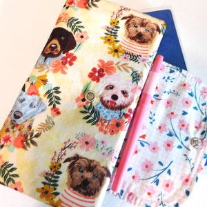 May include: A fabric planner cover with a dog-themed floral design. The cover features illustrations of various dog breeds surrounded by colorful flowers. A matching pen holder and a pink pen are also visible.