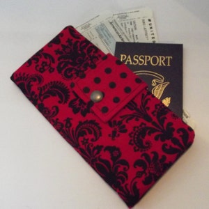 May include: A red and black fabric passport holder with a black floral design. The holder has a flap with black polka dots and a metal snap closure. A passport and airline tickets are visible inside.