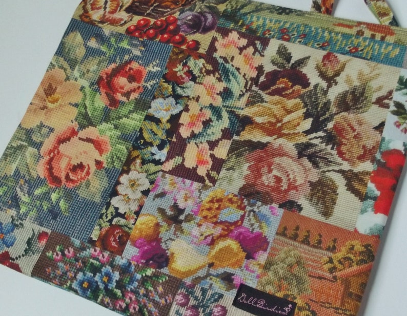 Pode incluir: Uma bolsa tote de patchwork com um design floral. A bolsa &eacute; feita de um tecido grosso e tecido e apresenta uma variedade de flores diferentes em tons de rosa, vermelho, amarelo e azul. A bolsa tem uma al&ccedil;a de couro marrom e um pequeno r&oacute;tulo que diz "Bell Indies".