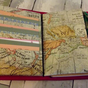 May include: A red leather-bound journal with a vintage world map design. The journal has a green pen and a brown ribbon attached to it. The journal has a pocket on the left side with several layers of decorative tape.
