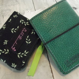 May include: Two small notebooks, one black with a green leaf pattern and the text "Bug. Emma." and the other green with a black elastic band.