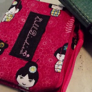 May include: A pink fabric pouch with a black label that says "Bellissima." The pouch has a floral pattern and features images of Japanese dolls with black hair and colorful clothing.