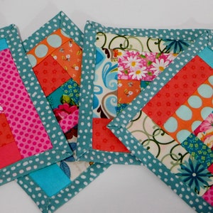 May include: Four handmade fabric coasters with a patchwork design. The coasters are made with a variety of colourful fabrics, including pink, orange, blue, and white. The coasters are edged with a teal fabric with white polka dots.