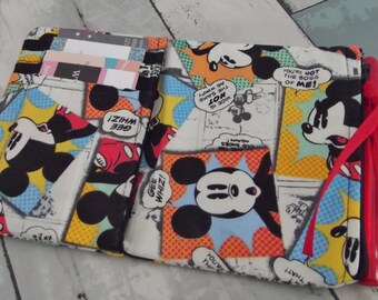 May include: Open wallet featuring a colorful comic strip design with Mickey Mouse illustrations. The wallet has multiple compartments for cards and cash, and a red ribbon closure. The design includes speech bubbles with phrases like "Gee Whiz!" and "You're not the boss of me!"