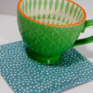 May include: A green ceramic mug with a white and green geometric pattern and an orange rim. The mug is sitting on a blue and white polka dot coaster.