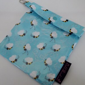 May include: A light blue, square pouch with a repeating pattern of white and yellow bees. The pouch has a silver-colored clasp and a black tag with the text "Bell Birdies". The pouch is closed with a snap.