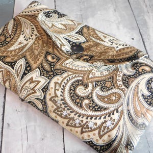 May include: A folded fabric clutch with a paisley pattern in shades of brown, beige, and black. The clutch is closed with a silver snap. The fabric has a soft, textured appearance.