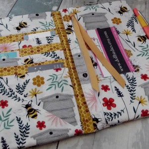 May include: Open fabric wallet with a bee and honeycomb pattern. The wallet has multiple card slots, a ribbon, and a pink pen. The background is white with bees, flowers, and beehive illustrations. The business card reads "www.dollbirdies.etsy.com".