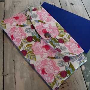 May include: A floral print wallet with a button closure. The wallet features a pattern of large pink flowers, green leaves, and berries on a white background. A blue object is visible in the background.