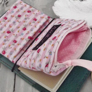 May include: A pink and white striped fabric wallet with a zipper closure and a pink ribbon. The wallet is open and has a small notebook inside.
