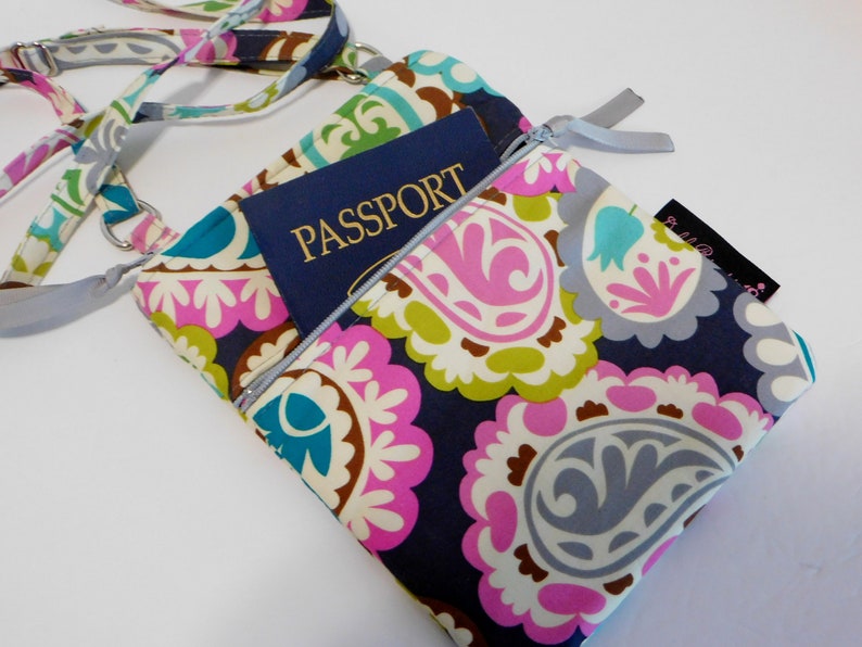 K&ouml;nnte beinhalten: Eine bunte Umh&auml;ngetasche mit Paisley-Muster, einer Rei&szlig;verschlusstasche und einem Reisepass im Inneren. Die Tasche hat einen grauen Riemen und ein kleines Etikett mit dem Text "Bella & Co."