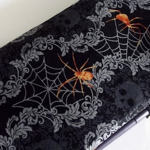 May include: Black fabric laptop sleeve with a repeating pattern of orange spiders, spiderwebs, and silver floral designs.