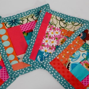 May include: Three colourful fabric squares with a teal polka dot border. The squares are made of patchwork fabric with various floral and geometric patterns in shades of pink, orange, blue, and green.