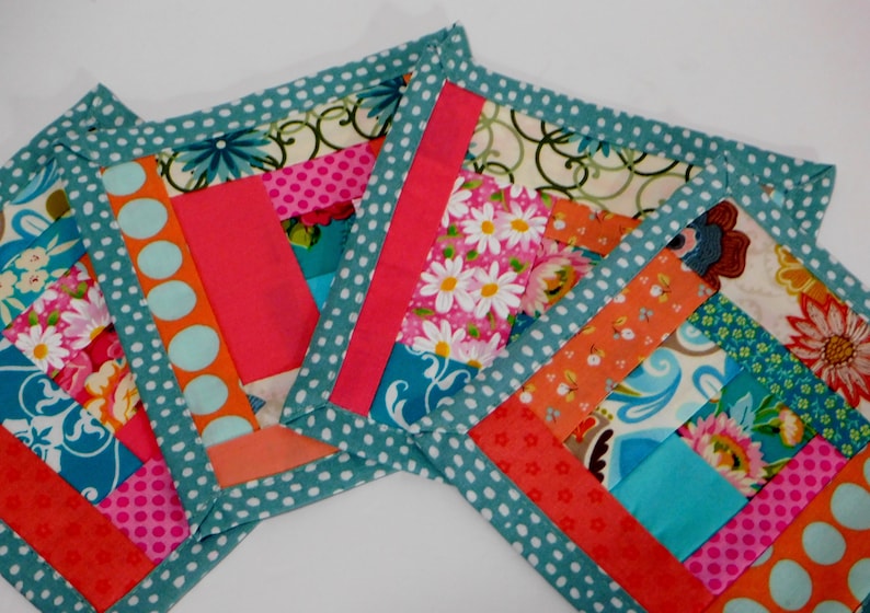 May include: Three colourful fabric squares with a teal polka dot border. The squares are made of patchwork fabric with various floral and geometric patterns in shades of pink, orange, blue, and green.