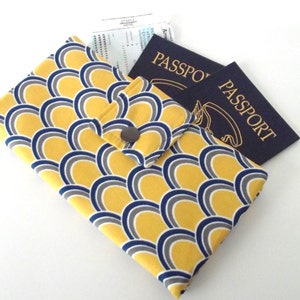 May include: A yellow, gray, and navy blue patterned passport holder with a snap closure. Two navy blue passports with gold lettering are next to the holder. A boarding pass is partially visible inside the holder.