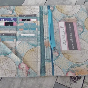 May include: Open fabric wallet with a world map design in shades of blue, beige, and pink. The wallet has multiple card slots, a zippered compartment, and a matching pen. The business card reads "Dollbirdies" and "www.dollbirdies.etsy.com".