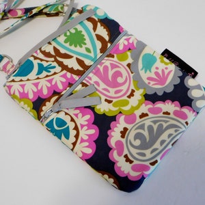K&ouml;nnte beinhalten: Eine kleine Umh&auml;ngetasche mit Paisley-Muster, silbernem Rei&szlig;verschluss und Trageriemen. Die Tasche hat einen dunkelblauen Hintergrund mit rosa, gr&uuml;nen und wei&szlig;en Paisley-Mustern.