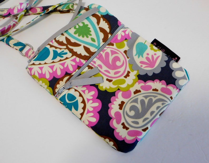 K&ouml;nnte beinhalten: Eine kleine Umh&auml;ngetasche mit Paisley-Muster, silbernem Rei&szlig;verschluss und Trageriemen. Die Tasche hat einen dunkelblauen Hintergrund mit rosa, gr&uuml;nen und wei&szlig;en Paisley-Mustern.