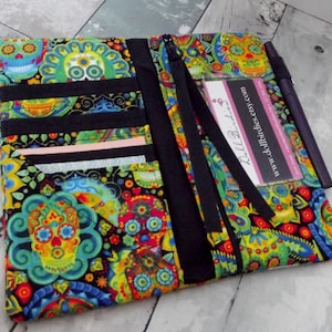 May include: A black zippered wallet with a colorful Day of the Dead pattern featuring skulls and flowers. The wallet has multiple card slots and a clear ID window. The text "Dollbirdies" and "www.dollbirdies.etsy.com" is printed on a white card inside the wallet.